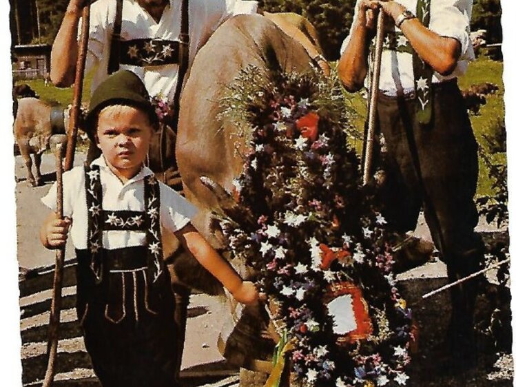 Drei festlich gekleidete Männer mit Trachten und Blumenkränzen posieren zusammen für ein Foto im Freien. | © Postkarte/Milz/1952