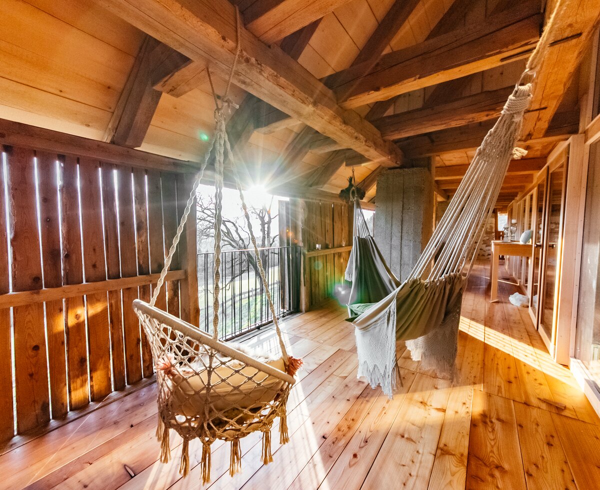 Hängestühle im Chalet Kaiser | © Urlaub am Bauernhof Kärnten / Daniel Gollner Gemütlicher Holzbalkon mit Hängesessel und Hängematte, umgeben von rustikalen Holzbalken und Fenstern, die einen Ausblick auf eine natürliche Landschaft gewähren. | © Urlaub am Bauernhof Kärnten / Daniel Gollner