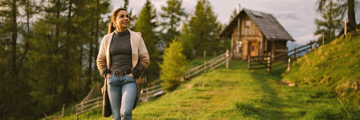 Eine Frau geht auf einer Wiese spazieren. Im Hintergrund erkennt man einen Wald und die Kleine Almhütte. | © Urlaub am Bauernhof / Daniel Gollner