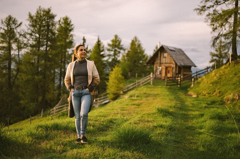 Eine Frau geht auf einer Wiese spazieren. Im Hintergrund erkennt man einen Wald und die Kleine Almhütte. | © Urlaub am Bauernhof / Daniel Gollner