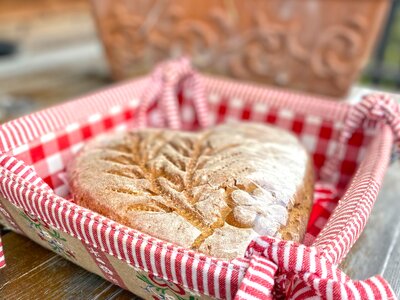 Brot Mechtenhütte | © Urlaub am Bauernhof Kärnten / Jasmin Kreulitsch Hausgebackener Brotlaib in dekorativer Holzschale, umwickelt mit karierter rot-weißer Serviette, eingebettet in eine blumige Umgebung. | © Urlaub am Bauernhof Kärnten / Jasmin Kreulitsch
