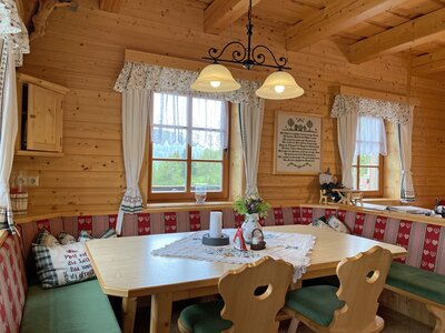 Esstisch Mechtenhütte | © Urlaub am Bauernhof Kärnten / Jasmin Kreulitsch Gemütliches Holzhaus mit rustikalem Interieur, großer Esstisch mit bestickten Sitzbänken, traditionelle Details wie Vorhänge und Kerzen, Blumen und ein Schild mit Spruch, eine gemütliche und einladende Atmosphäre. | © Urlaub am Bauernhof Kärnten / Jasmin Kreulitsch