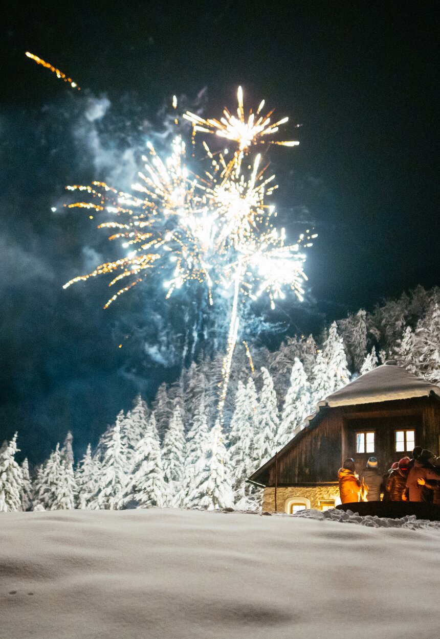 Lichterfunkeln über einer verschneiten Blockhütte, umgeben von schneebedeckten Bäumen, die das Bild in eine winterliche, feierliche Stimmung tauchen. | © Urlaub am Bauernhof / Daniel Gollner
