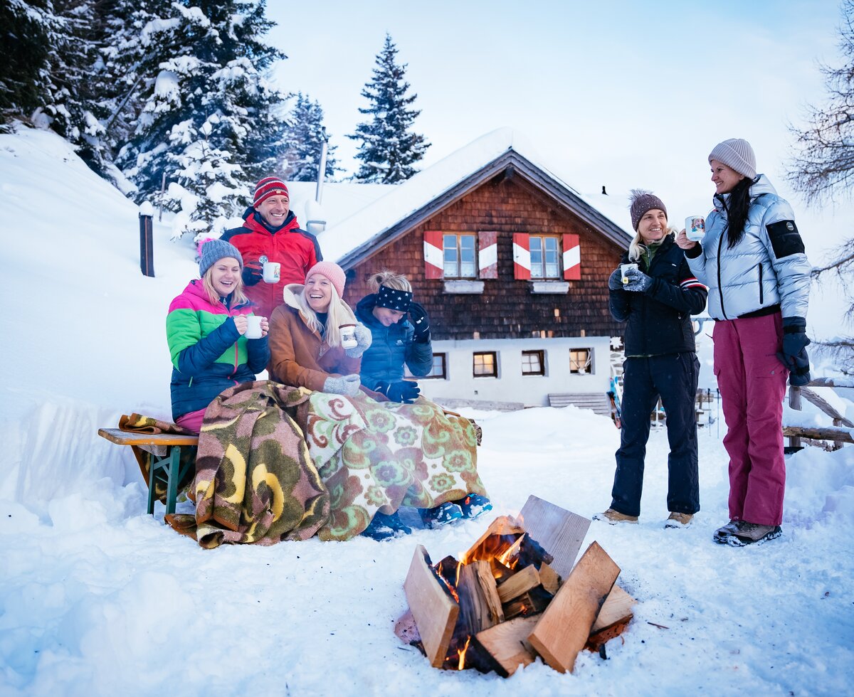Freunde sitzen bei der Feuerstelle | © Urlaub am Bauernhof Kärnten/ Daniel Gollner Freunde sitzen bei der Feuerstelle im Schnee vor der Hütte | © Urlaub am Bauernhof Kärnten/ Daniel Gollner