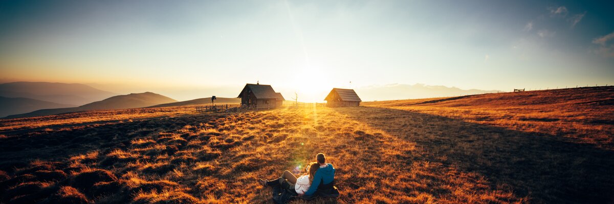 Paar sitzt vor der Hütte im Gras und genießt den Sonnenuntergang auf der Alm | © Urlaub am Bauernhof Kärnten/ Daniel Gollner 