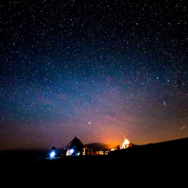 Beleuchtete Hütten in der Nacht, umgeben von einem sternenklaren Himmel in warmen Farben. Eine idyllische Szene in der Natur. | © Urlaub am Bauernhof Kärnten/ Daniel Gollner 