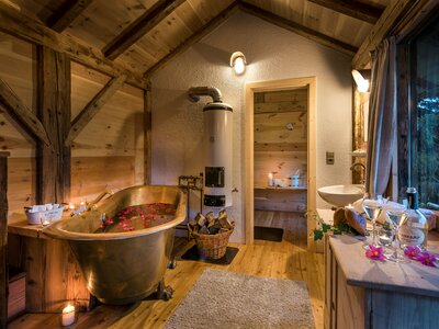 Gemütliche Holzhütte mit rustikalem Badezimmer, hölzernem Badewannen-Ensemble, Kamin und Badutensilien, umgeben von einer natürlichen Umgebung. | © Günter Standl 