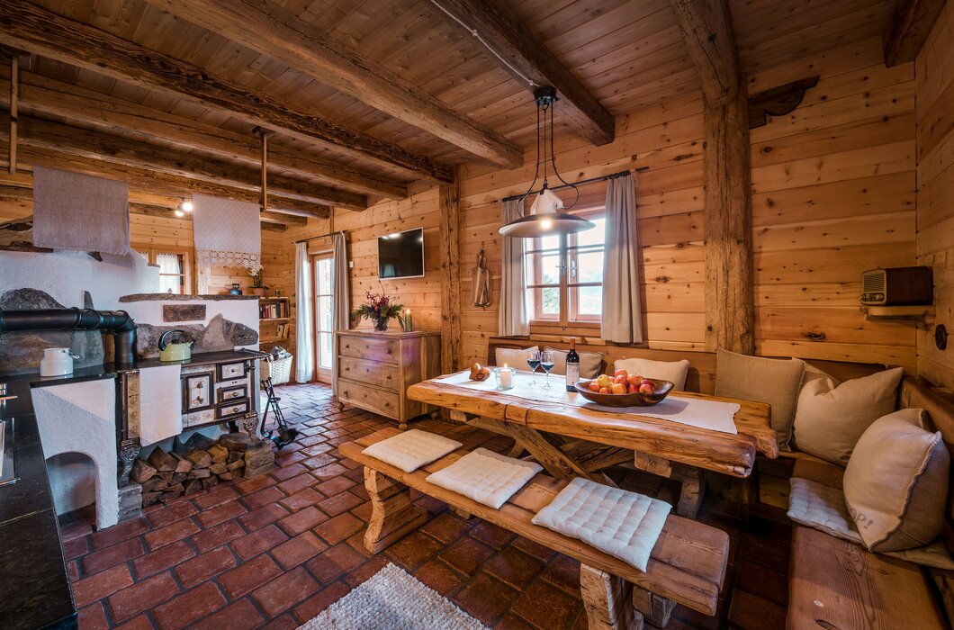 Gemütliches Holzinterieur mit rustikalem Esszimmertisch, einem Kaminofen und einer offenen Küche. Dekorative Details, wie Blumen und Naturalien, verleihen dem Raum eine charmante Atmosphäre. | © Günter Standl 