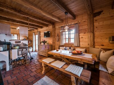 Gemütliches Holzinterieur mit rustikalem Esszimmertisch, einem Kaminofen und einer offenen Küche. Dekorative Details, wie Blumen und Naturalien, verleihen dem Raum eine charmante Atmosphäre. | © Günter Standl 