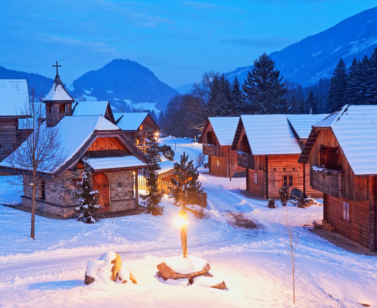 Landgut Moserhof im Winter | © Helene Hartweger Glanzer / Landgut Moserhof Eine verschneite Bergidylle mit malerischen Holzhäusern, einer Kirche und beleuchteten Weihnachtstannen. Eine abendliche Winterstimmung mit sanftem Lichtschein in der verschneiten Landschaft. | © Helene Hartweger Glanzer / Landgut Moserhof