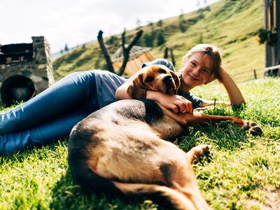 Mädchen und Hund in der Wiese | © Urlaub am Bauernhof Kärnten / Daniel Gollner Eine fröhliche Frau liegt auf einer grünen Wiese und umarmt ihren Hund liebevoll. Die Sonne scheint und eine einladende Berglandschaft bildet den Hintergrund. | © Urlaub am Bauernhof Kärnten / Daniel Gollner