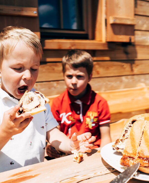 Kinder essen Kärntner Reindling | © Urlaub am Bauernhof Kärnten / Daniel Gollner Ein Kind isst einen Kärntner Reindling vor der Almhütte im Sommer | © Urlaub am Bauernhof Kärnten / Daniel Gollner