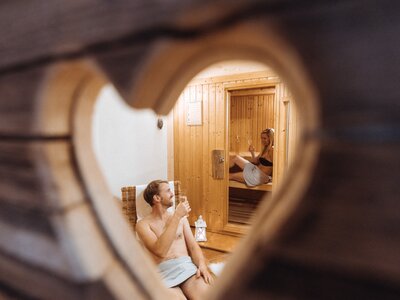 Sauna mit Mann und Frau, die auf unterschiedlichen Ebenen entspannen. Die Szene suggeriert eine entspannte, intime Atmosphäre. | © Urlaub am Bauernhof / Achim Mandler