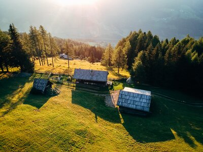 Eine malerische ländliche Landschaft mit Berghütten, umgeben von Nadelwäldern, einer Wiese und Sonnenlicht, das die Szene erleuchtet. | © Urlaub am Bauernhof Kärnten / Daniel Gollner