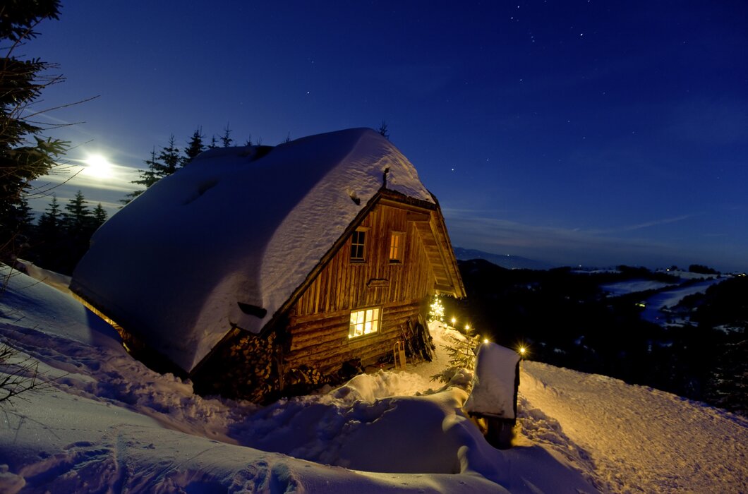 Kärntner Alm bei Nacht im Winter | © Urlaub am Bauernhof/ Tom Lamm Eine verschneite Berghütte mit beleuchteten Fenstern und einer schneebedeckten Umgebung unter einem sternenübersäten Nachthimmel. | © Urlaub am Bauernhof/ Tom Lamm