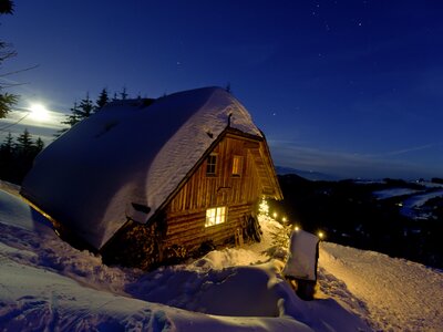 Kärntner Alm bei Nacht im Winter | © Urlaub am Bauernhof/ Tom Lamm Eine verschneite Berghütte mit beleuchteten Fenstern und einer schneebedeckten Umgebung unter einem sternenübersäten Nachthimmel. | © Urlaub am Bauernhof/ Tom Lamm