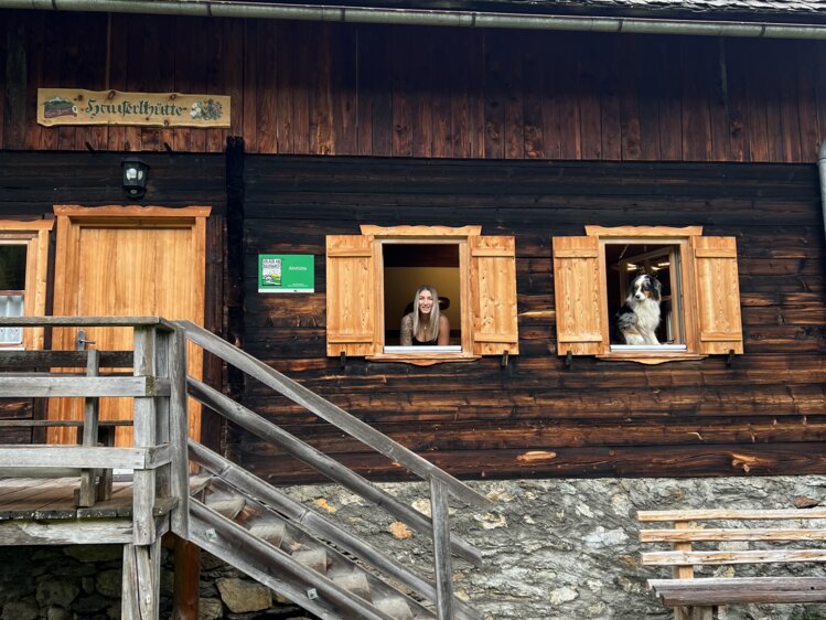 Altes Holzhaus mit Fensterläden, Aufbauten aus Holzkisten und Leiter angelehnt an der Fassade, umgeben von Grün. | © Urlaub auf der Alm / Julia Winkler