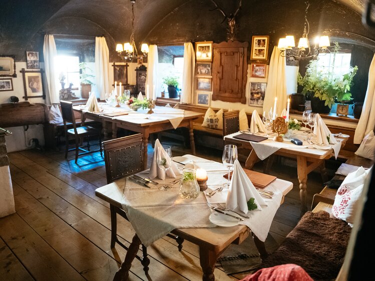 Gemütlicher Essraum mit rustikalem Holztisch, Stühlen und Dekorationen wie Kerzen, Bilder und Blumen. Behagliche, traditionelle Atmosphäre mit hellen Vorhängen und Beleuchtung. | © Urlaub am Bauernhof / Daniel Gollner