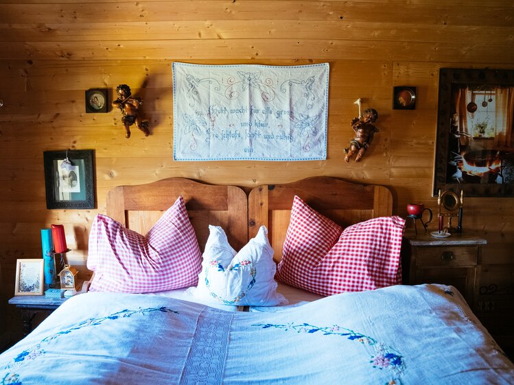 Ein gemütliches Schlafzimmer mit hölzerner Einrichtung, beblümter Bettwäsche und dekorativen Wandornamenten. Die Möbel und Textilien vermitteln einen traditionellen, ländlichen Charme. | © Urlaub am Bauernhof / Daniel Gollner