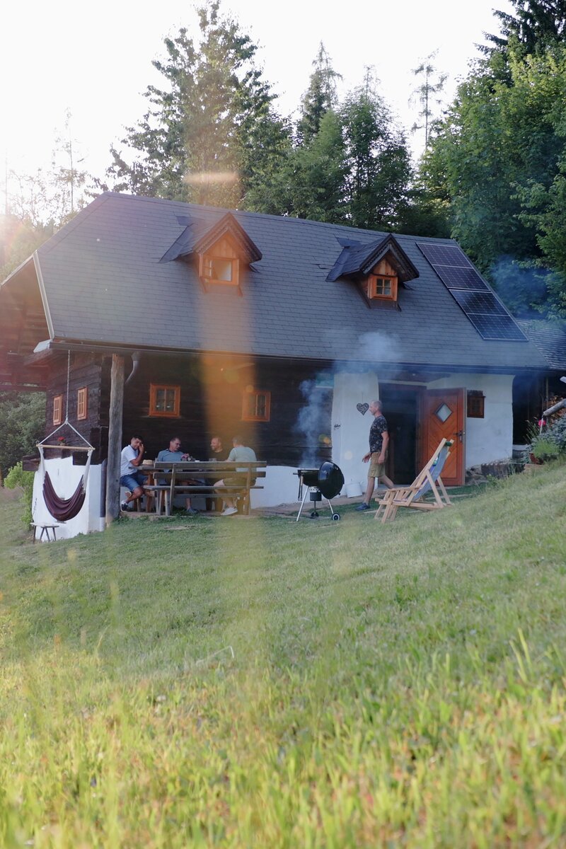 Auf einer idyllischen Almhütte umgeben von Wiesen und Wäldern wird gemeinsam gegrillt. Freunde sitzen auf der Veranda zusammen und reden. | © Urlaub am Bauernhof / Daniel Gollner