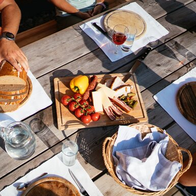 Almjausen auf einer Hütte in der Steiermark | © Urlaub am Bauernhof Steiermark / Daniel Gollner Gemütliches Holztisch-Picknick im Freien mit Brot, Käse, Wurst, Oliven und Gläsern für Wein oder Schnaps. Frische Früchte und Gemüse sowie Besteck und Servietten vervollständigen die Tischausstattung. | © Urlaub am Bauernhof Steiermark / Daniel Gollner