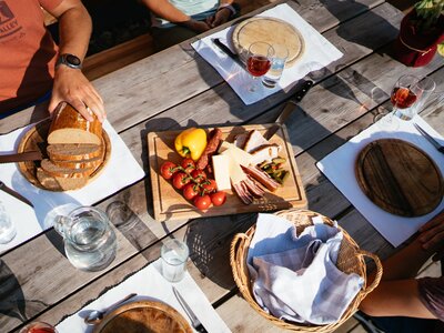 Almjausen auf einer Hütte in der Steiermark | © Urlaub am Bauernhof Steiermark / Daniel Gollner Gemütliches Holztisch-Picknick im Freien mit Brot, Käse, Wurst, Oliven und Gläsern für Wein oder Schnaps. Frische Früchte und Gemüse sowie Besteck und Servietten vervollständigen die Tischausstattung. | © Urlaub am Bauernhof Steiermark / Daniel Gollner