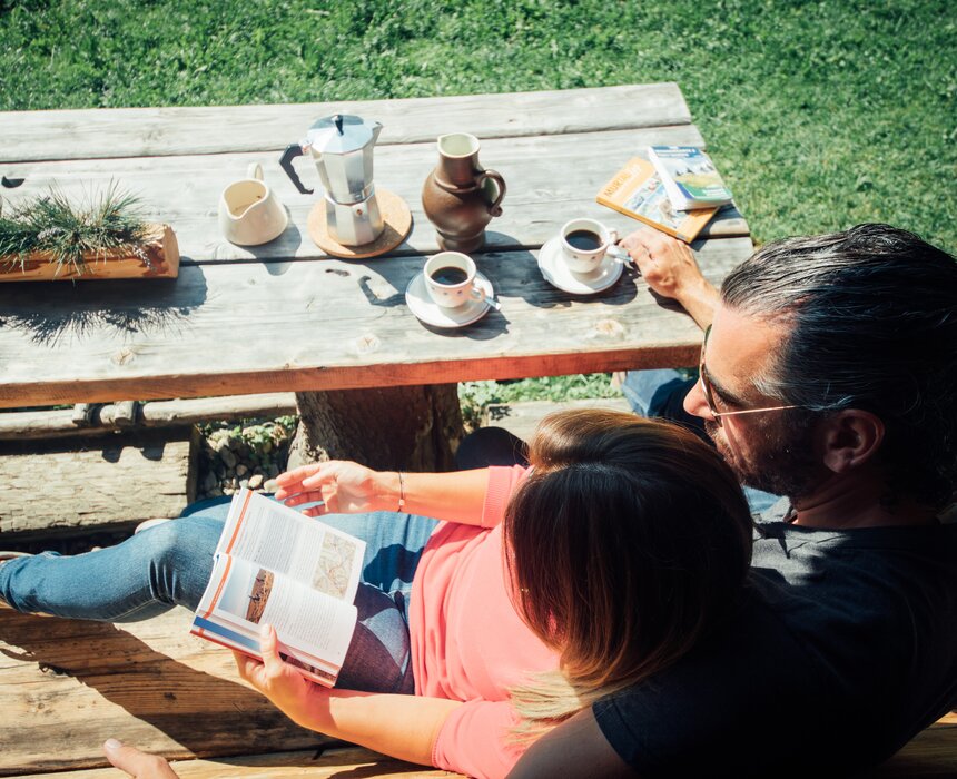 Zwei Personen genießen Kaffee und Lektüre auf einer hölzernen Terrasse inmitten einer grünen Umgebung. | © Urlaub am Bauernhof Steiermark / Daniel Gollner 