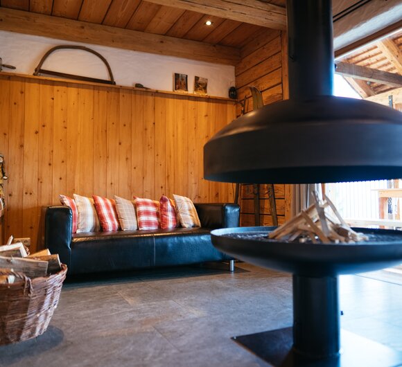 Gemütliches Holzhütten-Interieur mit Sofa, Kaminofen und Holzkörben. Ein modernes, rustikales Ambiente, das zu einem entspannenden Aufenthalt einlädt. | © Urlaub am Bauernhof Steiermark / Daniel Gollner