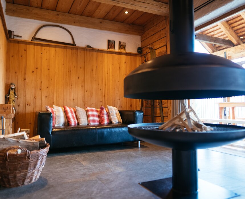 Gemütliches Holzhütten-Interieur mit Sofa, Kaminofen und Holzkörben. Ein modernes, rustikales Ambiente, das zu einem entspannenden Aufenthalt einlädt. | © Urlaub am Bauernhof Steiermark / Daniel Gollner