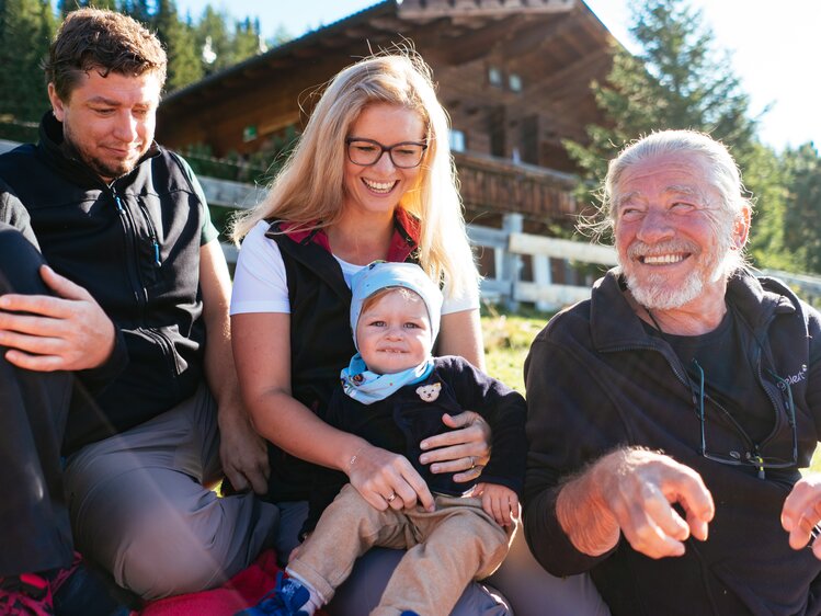 Lächelnde Familie im Freien, bestehend aus einem Paar Erwachsenen und einem Kleinkind, vor einer hölzernen Gebirgslandschaft. | © Urlaub am Bauernhof Tirol / Daniel Gollner 