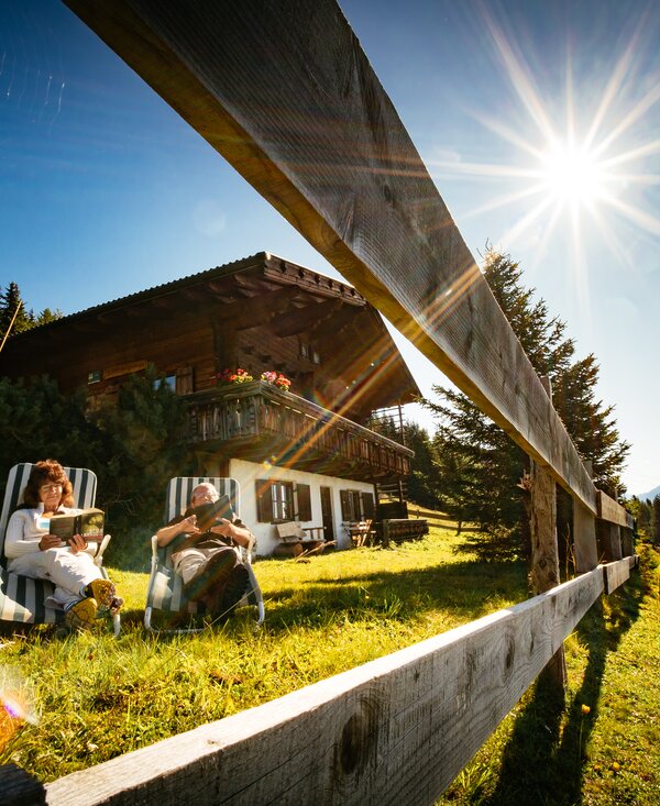Grosseltern entspannen vor der Hütte | © Urlaub am Bauernhof Tirol / Daniel Gollner Zwei ältere Leute lesen vor der Almhütte im Liegestuhl | © Urlaub am Bauernhof Tirol / Daniel Gollner