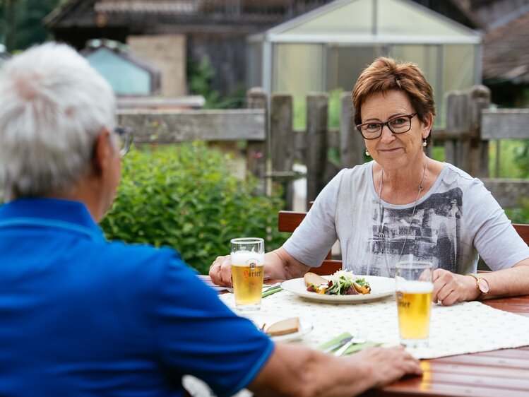 Eine Frau und ein Mann sitzen im Freien und essen gemeinsam. | © Urlaub am Bauernhof Kärnten/ Angelina Tschische
