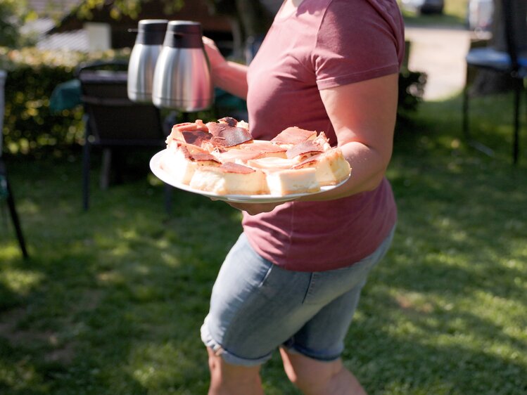 Person hält eine Platte mit Getränken und Snacks im Garten bei Sonnenlicht.