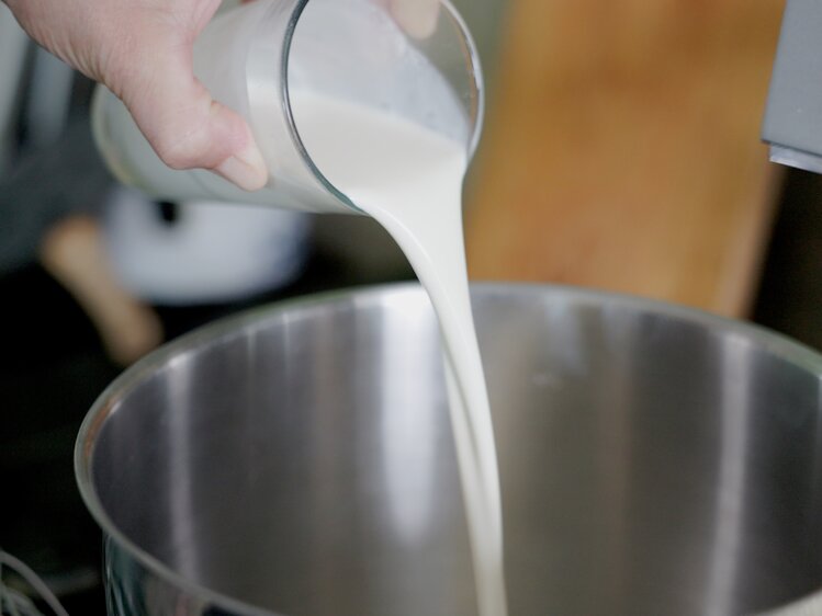 Person gießt Milch in eine Küchenmaschine oder einen Mixer, um sie für ein Rezept vorzubereiten.