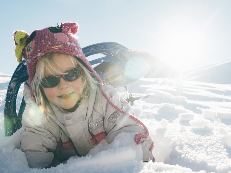 Mädchen liegt im Schnee mit Skianzug | © Urlaub am Bauernhof Kärnten / Daniel Gollner