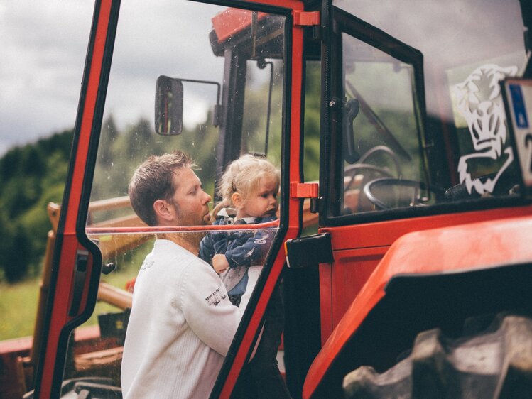 Mädchen und Mann stehen beim Traktor | © Urlaub am Bauernhof Kärnten / Daniel Gollner