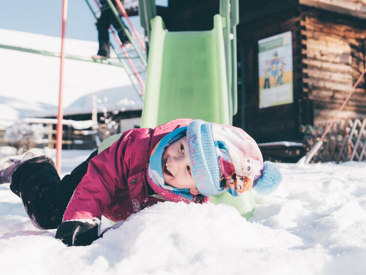 Mädchen liegt vor der Rutsche im Schnee | © Urlaub am Bauernhof Kärnten / Daniel Gollner