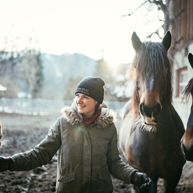 Ida Winkler vom Pfeiferhof | © Urlaub am Bauernhof Kärnten / Daniel Gollner Frau steht mit Pferden im Auslauf | © Urlaub am Bauernhof Kärnten / Daniel Gollner