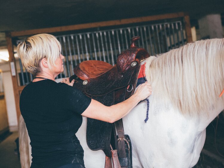 Frau sattelt das Pferd im Stall | © Urlaub am Bauernhof Kärnten / Daniel Gollner