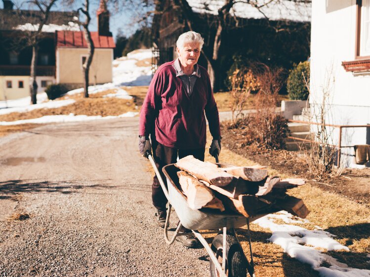 Bäuerin fährt mit dem Holz in der Scheibtruhe | © Urlaub am Bauernhof Kärnten / Daniel Gollner