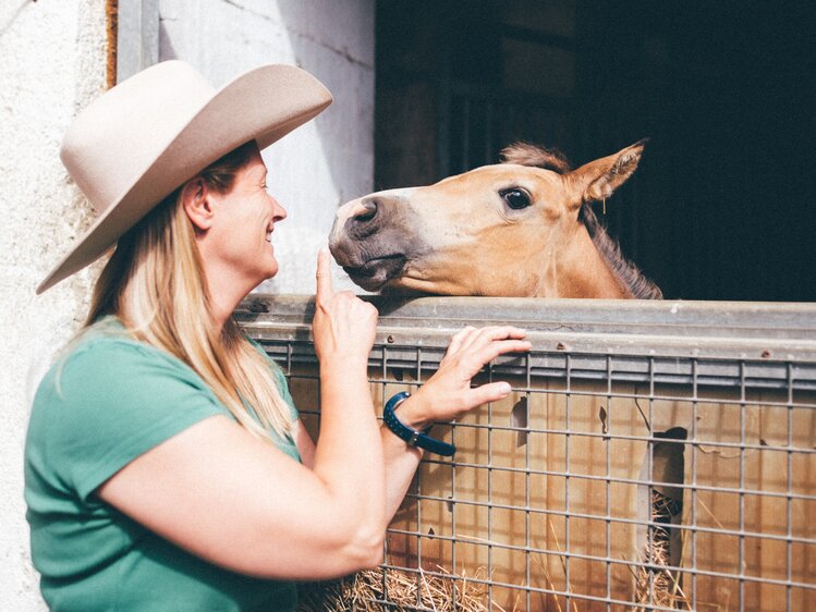 Frau steht vor der Pferdebox und Pferd schaut heraus | © Urlaub am Bauernhof Kärnten / Daniel Gollner