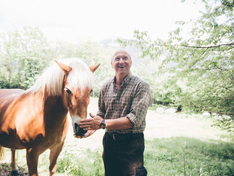 Mann steht bei Pferd und greift auf den Kopf des Pferdes | © Urlaub am Bauernhof Kärnten / Daniel Gollner