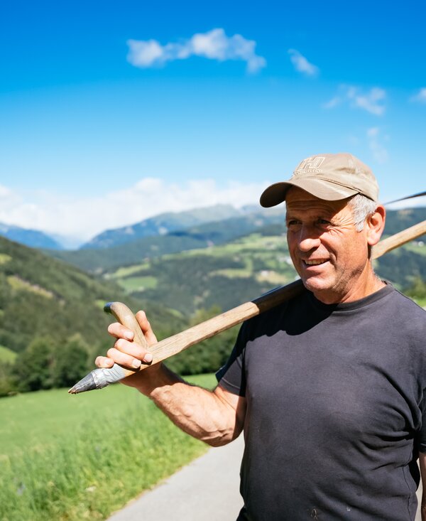 Sepp Striedinger hat die Sense geschultert | © Urlaub am Bauernhof Kärnten/ Daniel Gollner Bauer hat die Sense geschultert und steht auf der Straße | © Urlaub am Bauernhof Kärnten/ Daniel Gollner