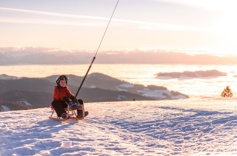 Kind auf Schlitten im Abendlicht im Schnee | © Michael Stabentheiner / Tourismusregion Mittelkärnten