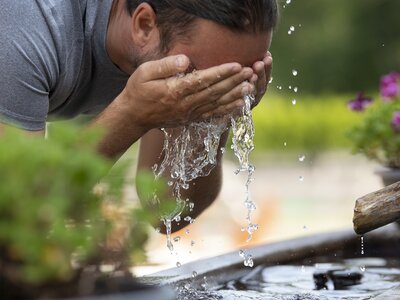Mann erfrischt sich nach dem Wandern mit kühlem Wasser vom Brunnen | © Urlaub am Bauernhof Oberösterreich / Andreas Hofer