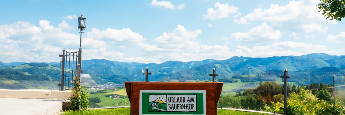 Liege mit der Aufschrift "Urlaub am Bauernhof" und Panoramablick auf den Nationalpark Kalkalpen | © Urlaub am Bauernhof Oberösterreich / Daniel Gollner