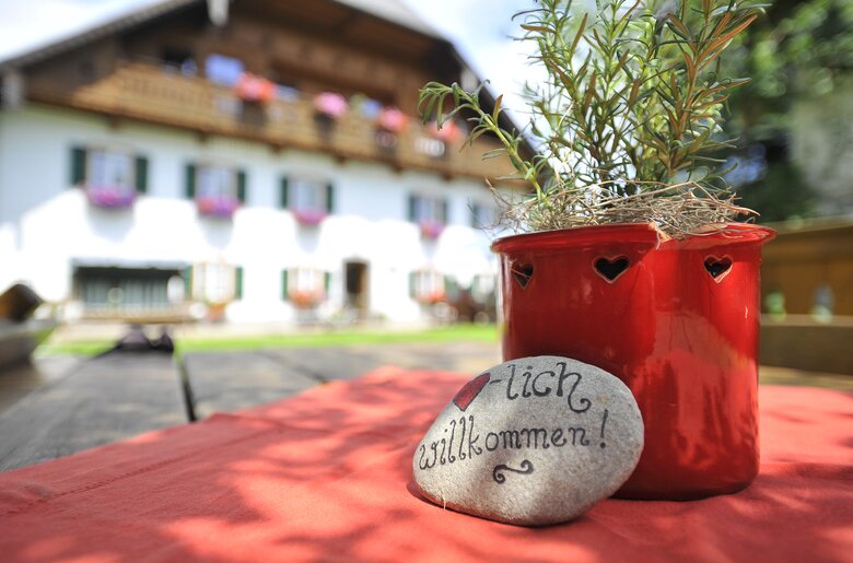 Bemalter Stein mit "herzlich willkommen" liegt auf dem Tisch vor dem Bauernhaus | © Urlaub am Bauernhof Oberösterreich / Ralph Fischbacher