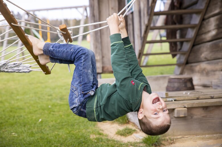 Bub hängt kopfüber am Spielplatz und lacht | © Urlaub am Bauernhof Oberösterreich / Puremotions Photography