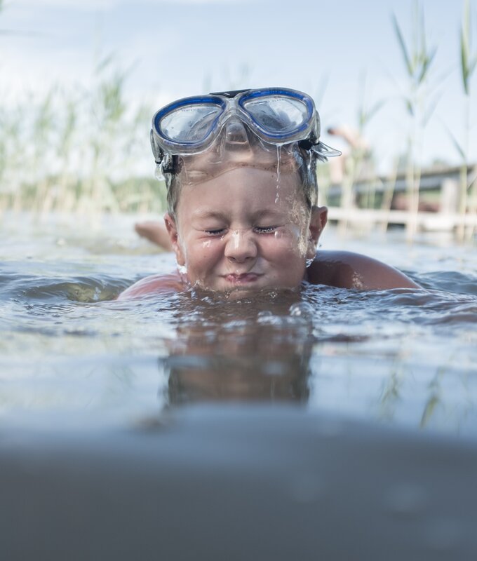 Bub mit Taucherbrille badet im See und prustet ins Wasser | © Urlaub am Bauernhof Oberösterreich / Robert Maybach
