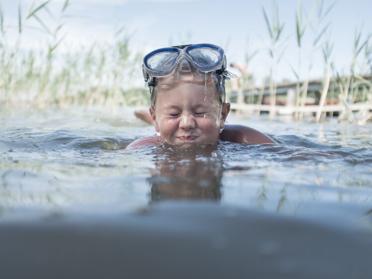 Bub mit Taucherbrille badet im See und prustet ins Wasser | © Urlaub am Bauernhof Oberösterreich / Robert Maybach
